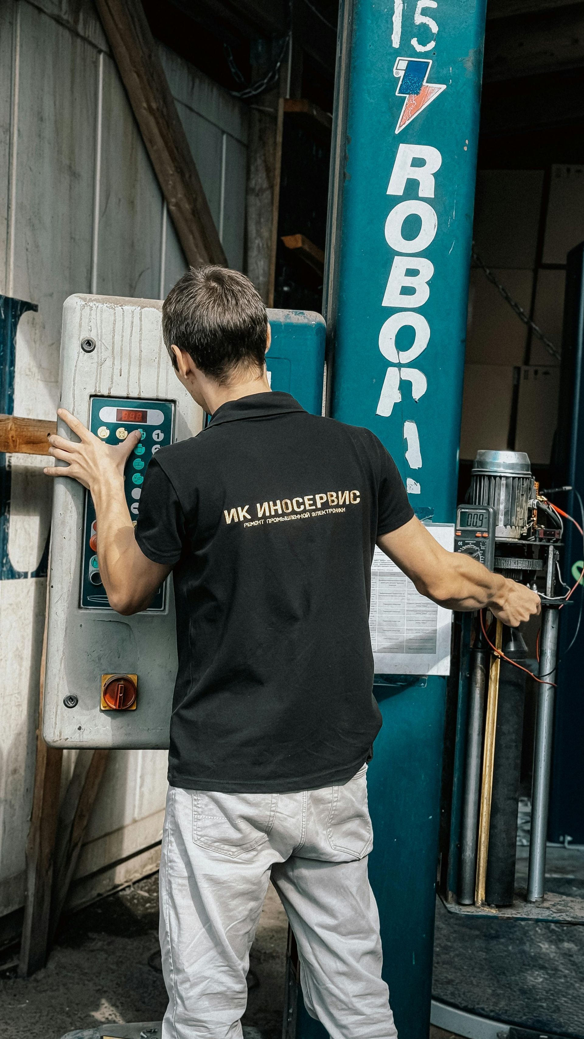 Man in black shirt operating machinery control panel in workshop.
