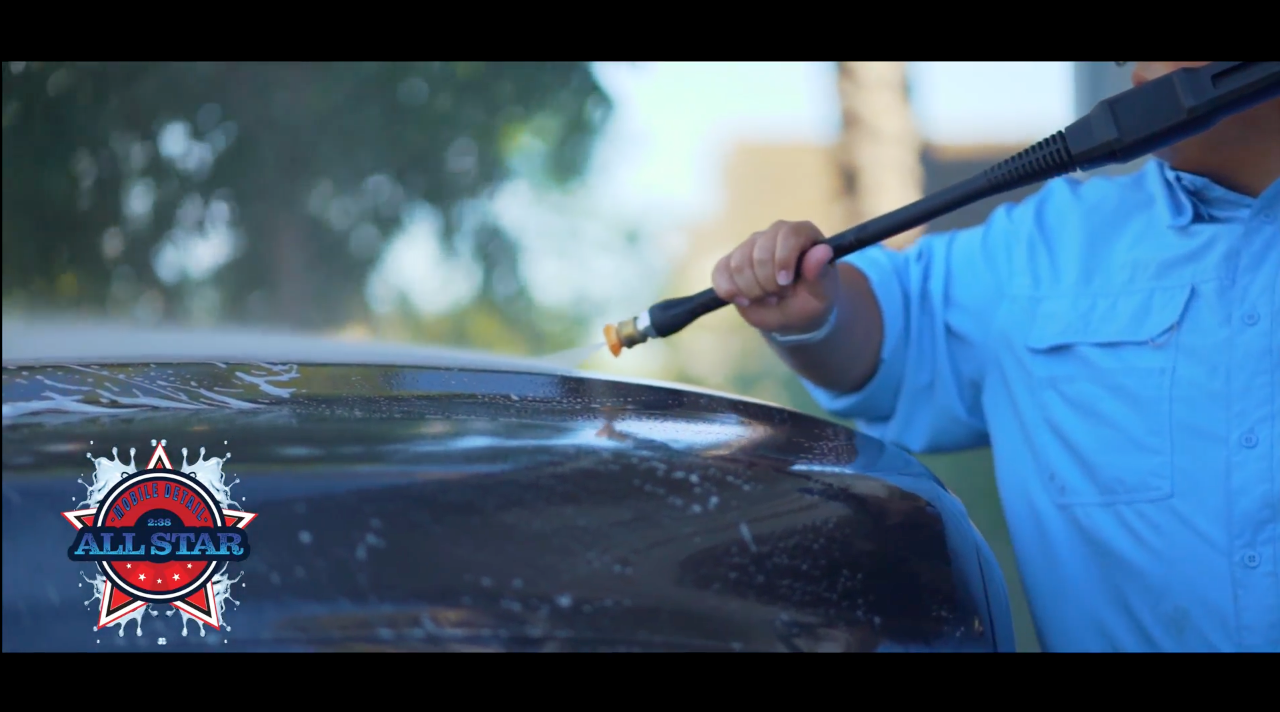 A man is using a high pressure washer to clean a car