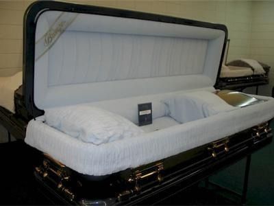 Open black coffin with white interior, a pillow, and a small box.