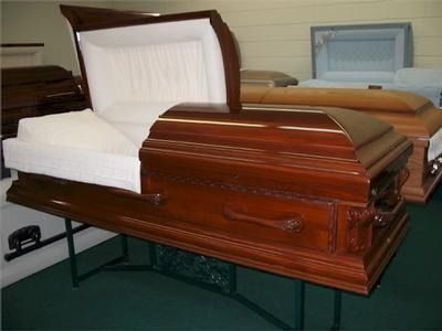 Open wooden casket, brown finish, white interior, on display.