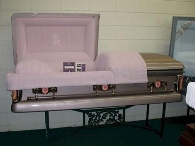 Open pink casket on display, showcasing interior fabric and hardware in a showroom setting.