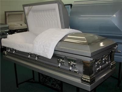 Silver casket with open lid, white interior, on a metal table, in a showroom.