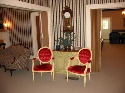 Two red velvet chairs face a cabinet with a grandfather clock, in a room with striped wallpaper and open doorways.