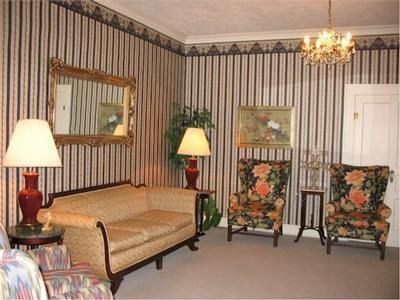 Formal living room with striped wallpaper, sofa, floral armchairs, lamps, and a chandelier.