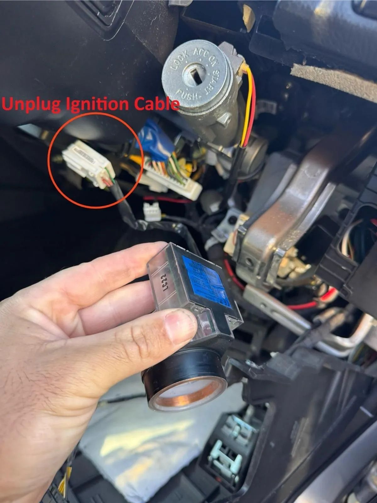 Hand holding a car ignition switch behind a dashboard, with a red-circled unplugged ignition cable.