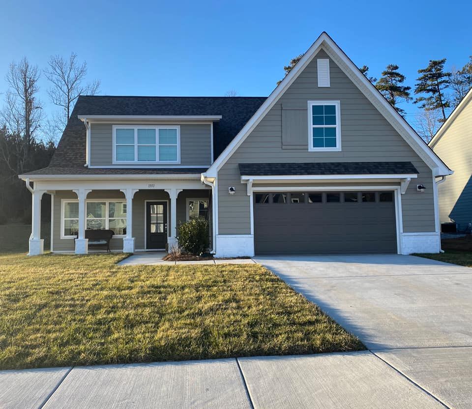 Gray house with black roof, covered porch, and attached garage on a sunny day.