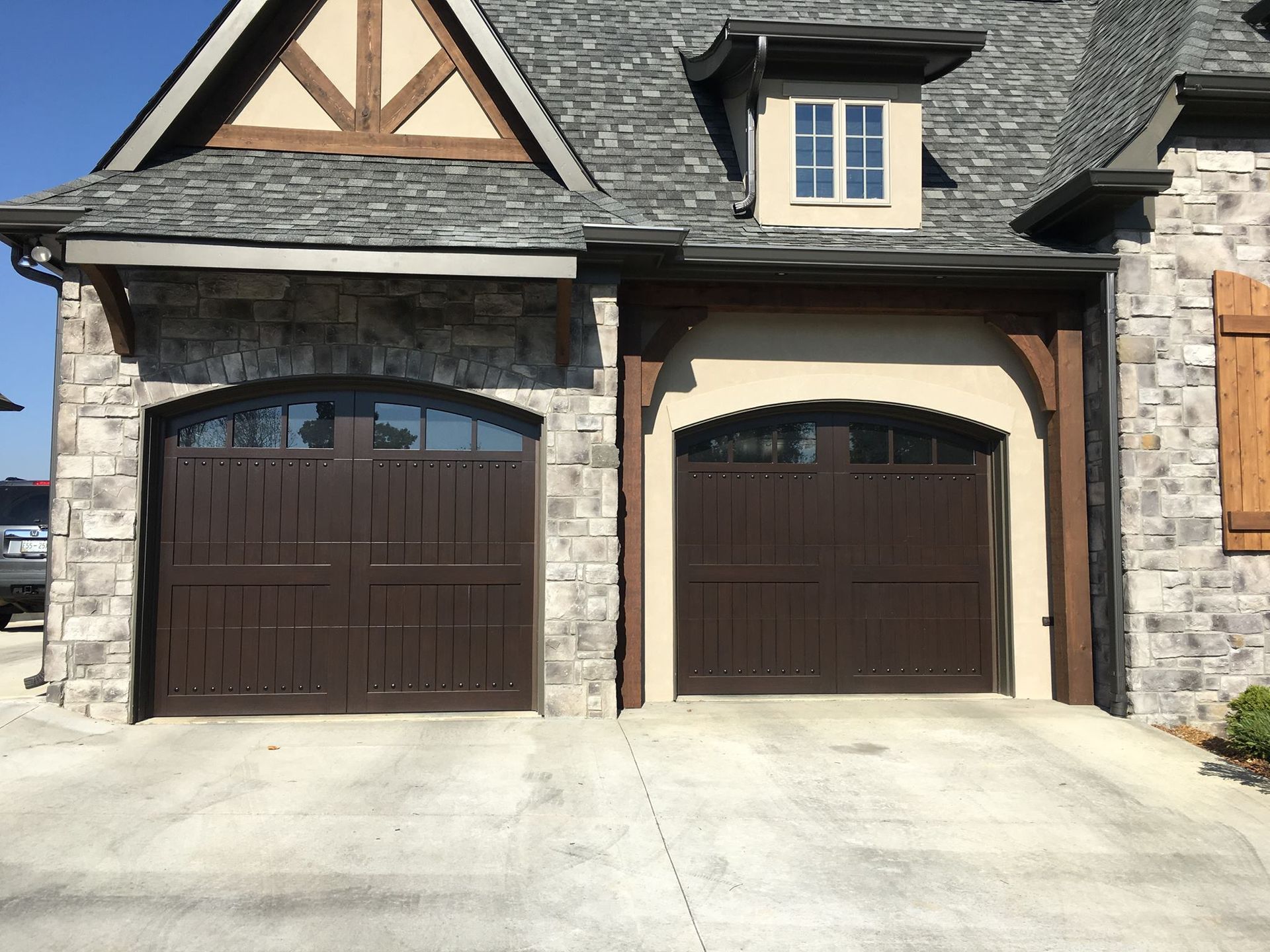 Two brown garage doors with arched windows in a stone and tan-colored facade building.