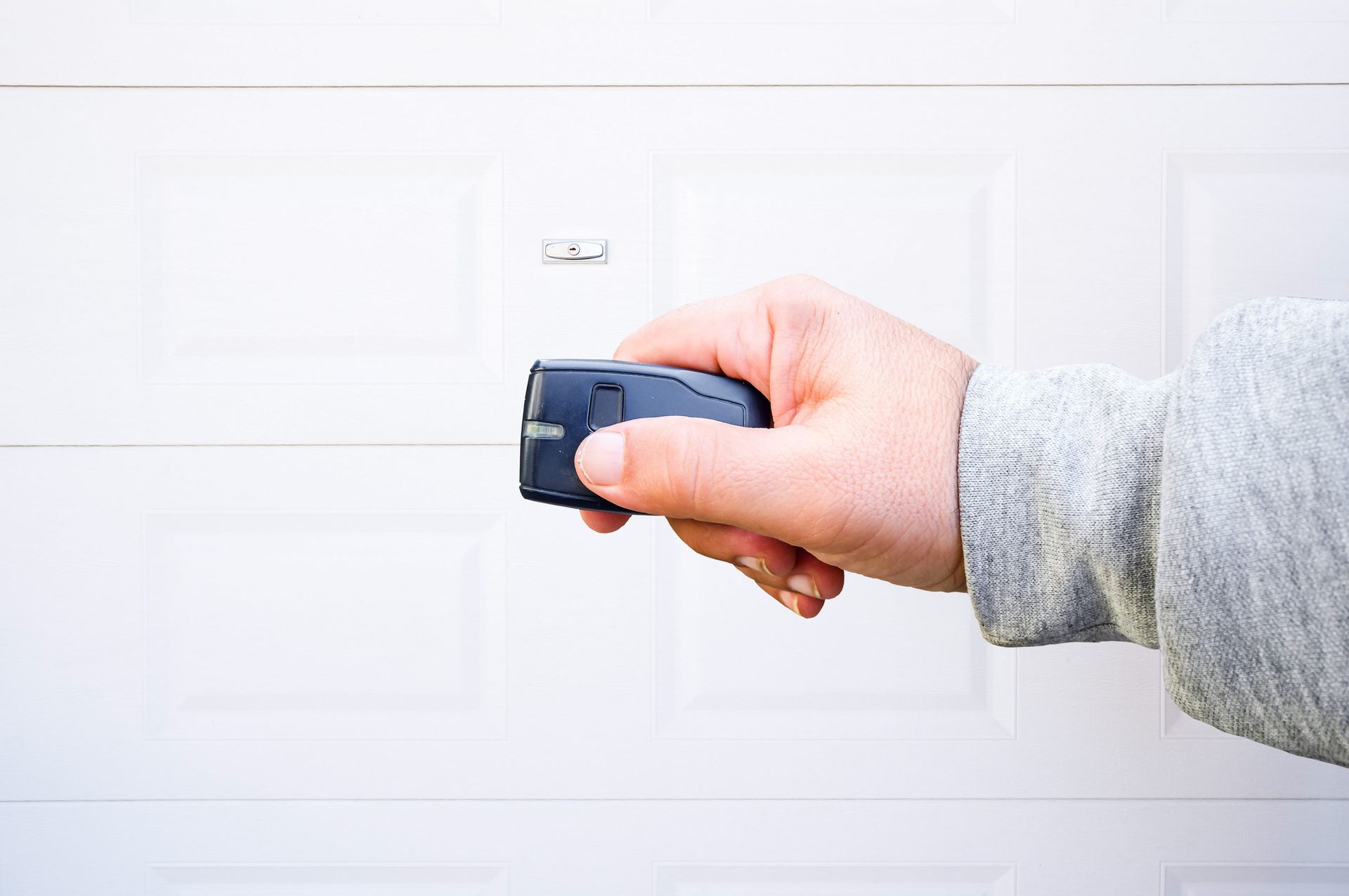 Hand holding a black garage door opener, aiming it at a white garage door.
