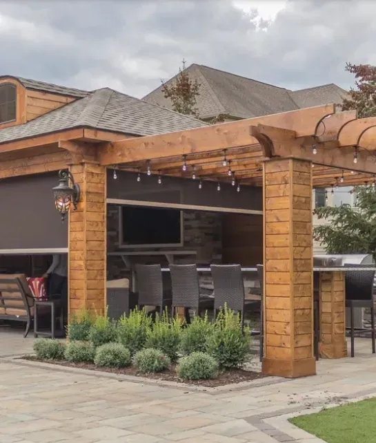 Two-story brick house with dark roof and tan siding, exterior sunshade, and a wooden deck.