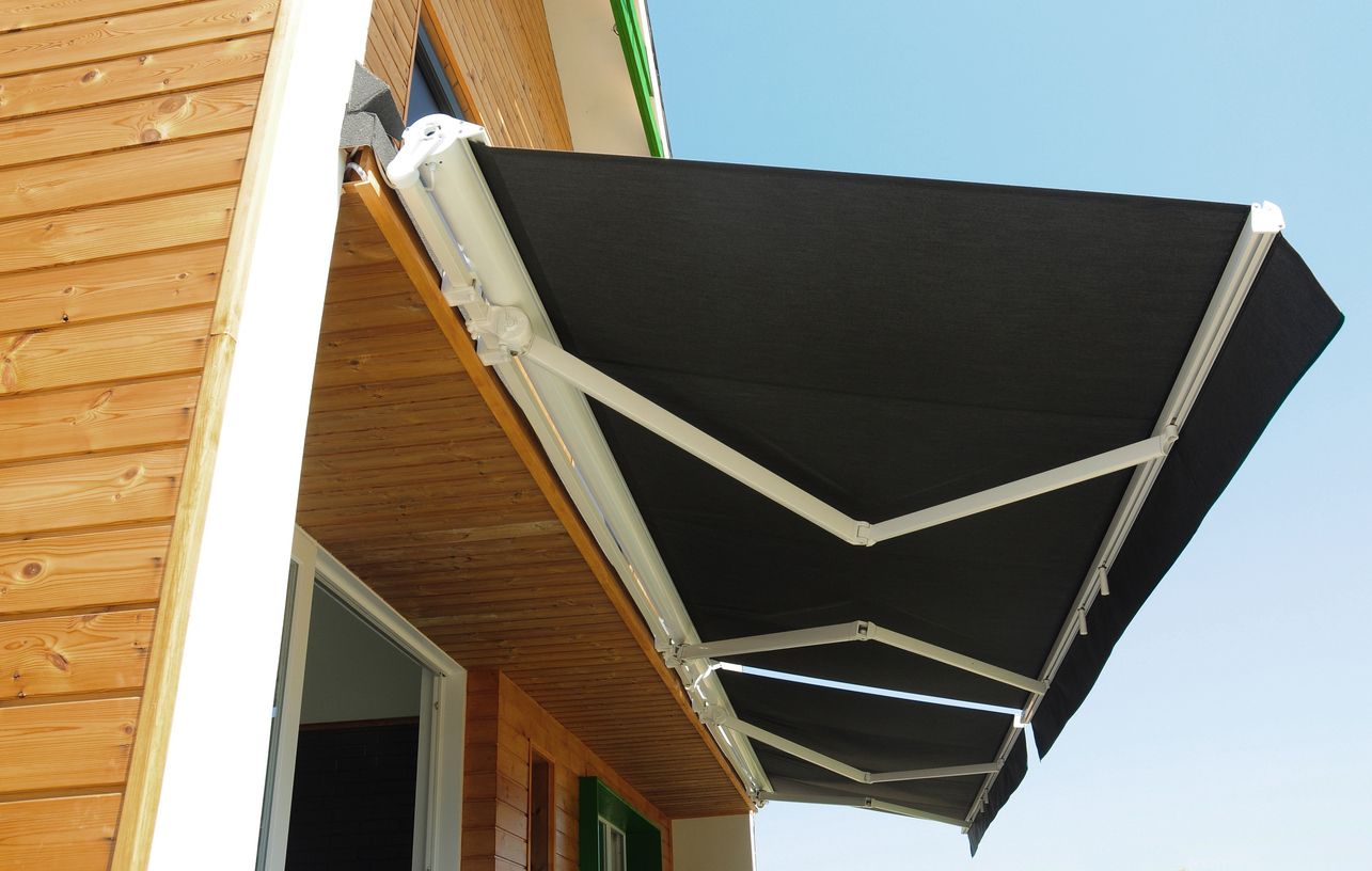 Black retractable awning extended from a wooden building, bright sky.