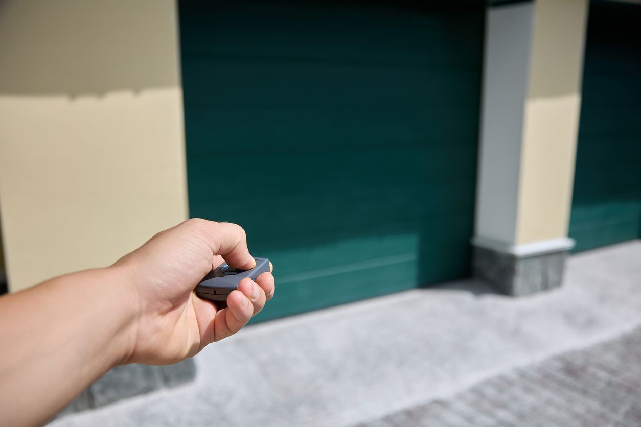 Hand holding a garage door opener, pointing at a green garage door.