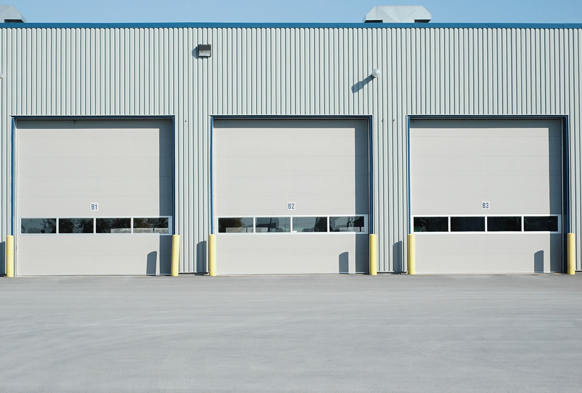 Three closed loading dock doors on a gray industrial warehouse facade