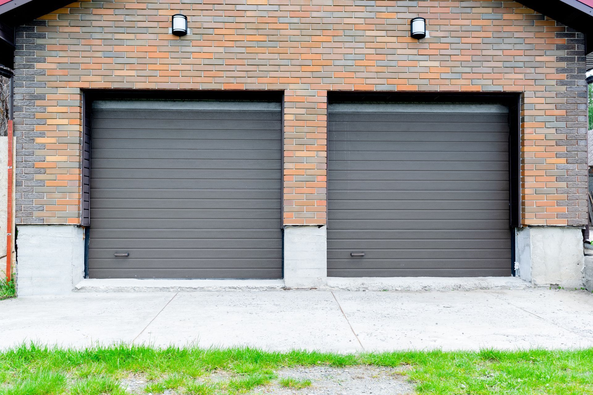 Two brown garage doors on a brick building with concrete foundation.