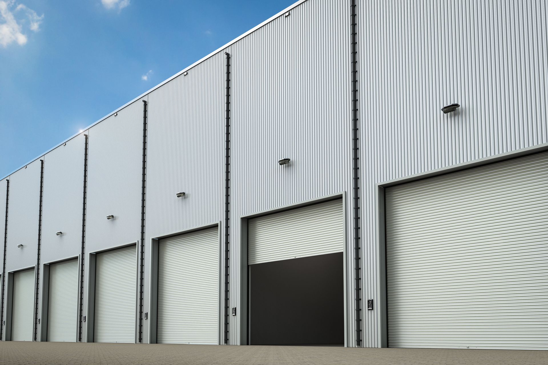 Exterior of a corrugated metal warehouse with several open and closed bay doors against a blue sky.