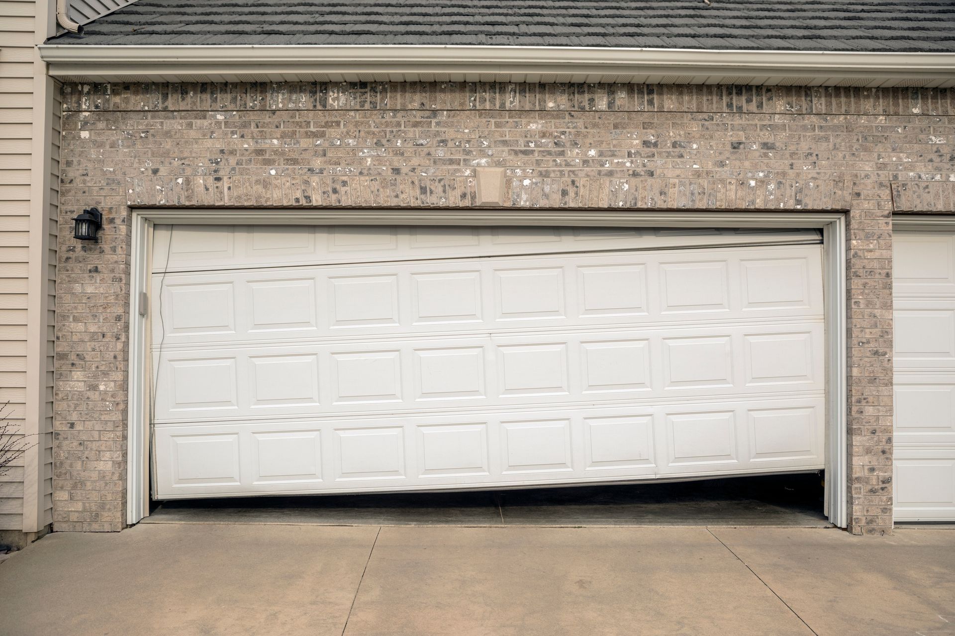 Garage door, partially open and tilted, set in a brick wall.