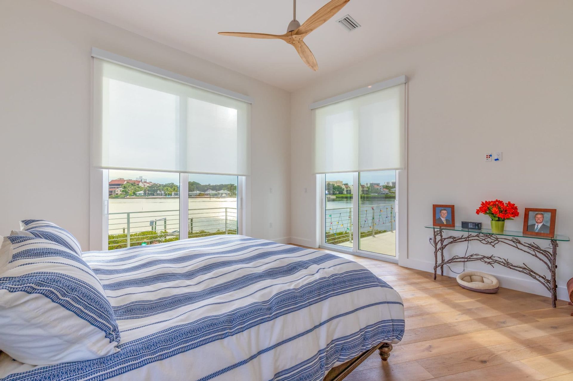 Bedroom with a bed, windows, and water view. Blue and white striped bedding, neutral walls, wood floor.