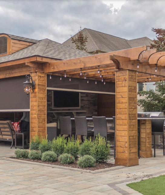 Outdoor patio with pergola, bar, TV, and seating under a cloudy sky.