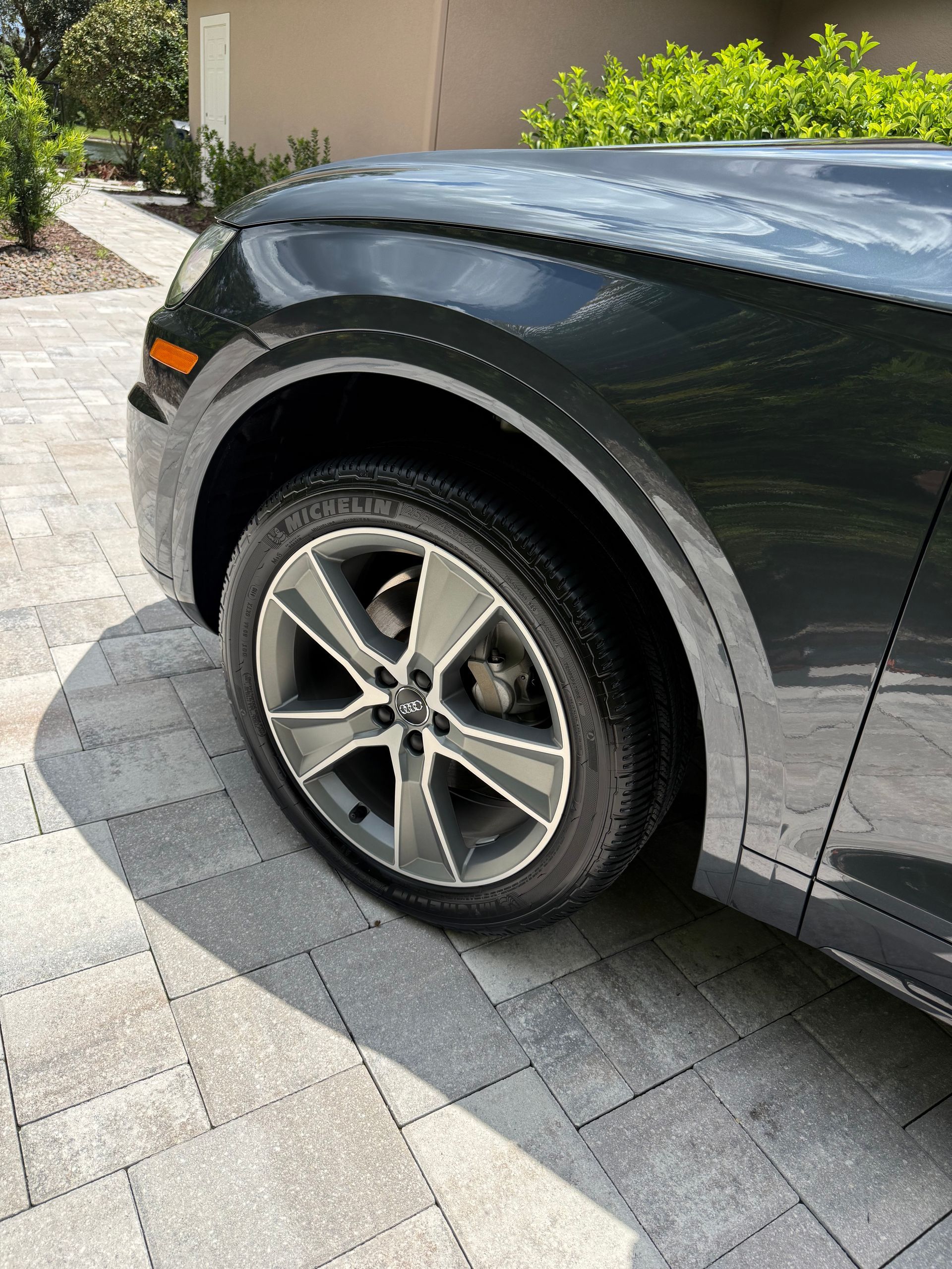 A black car is parked on a brick driveway.