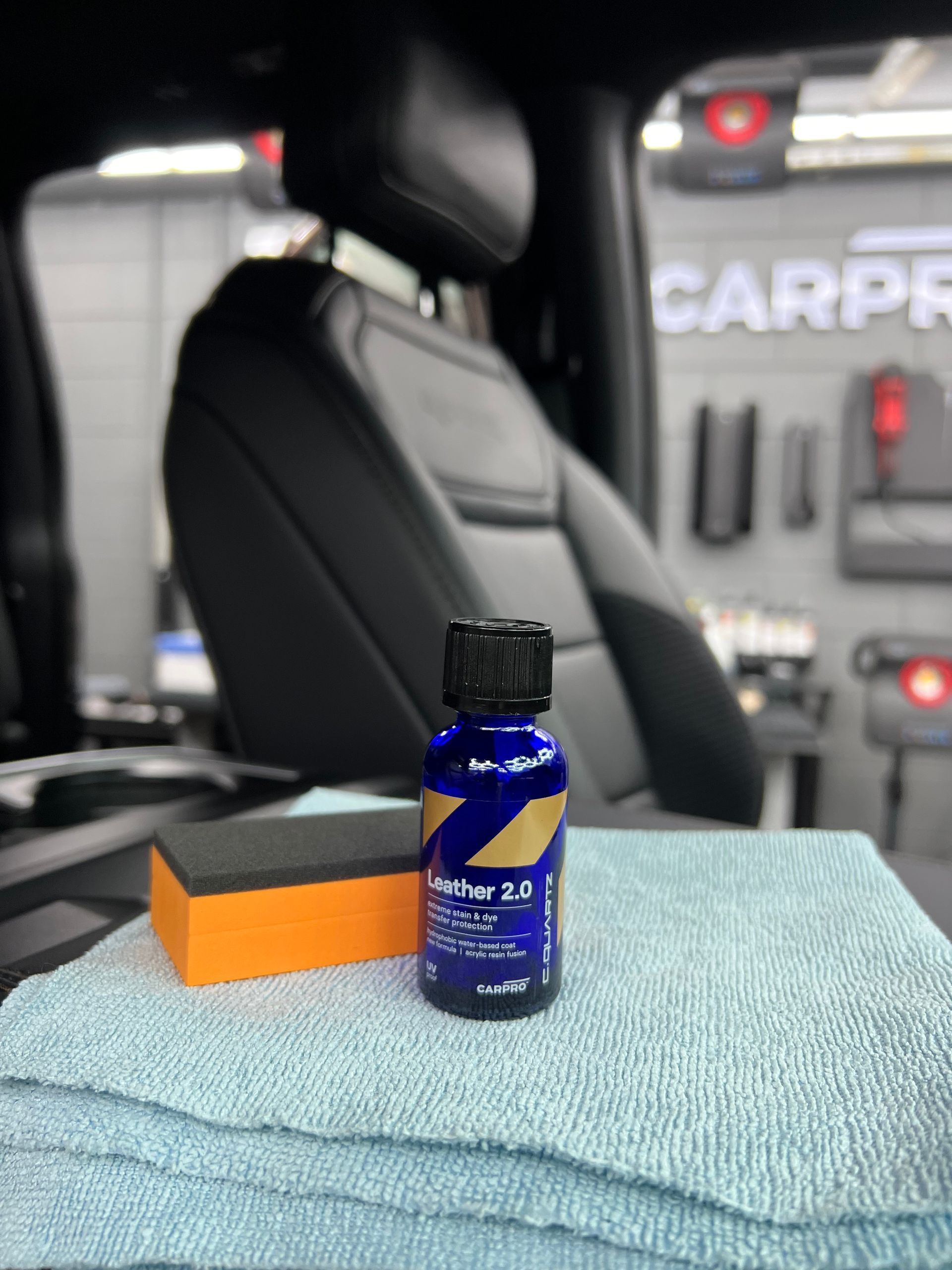 A bottle of car polish sits on a towel next to a sponge