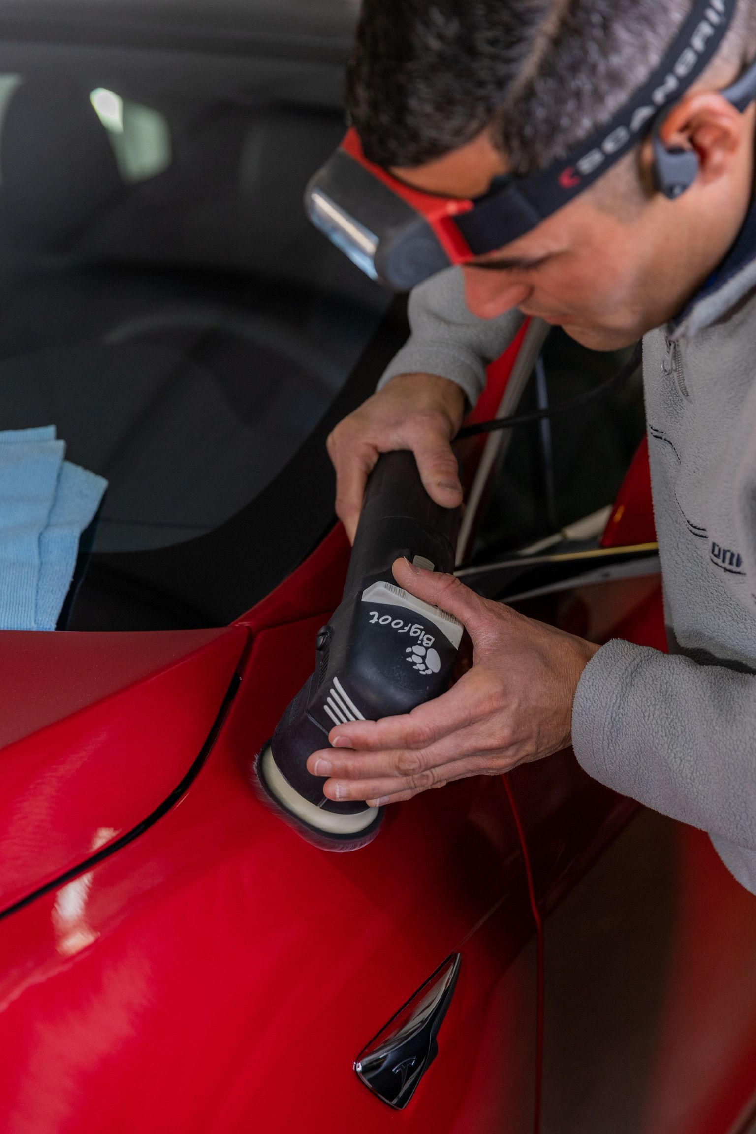 A man is polishing a red car with a machine.