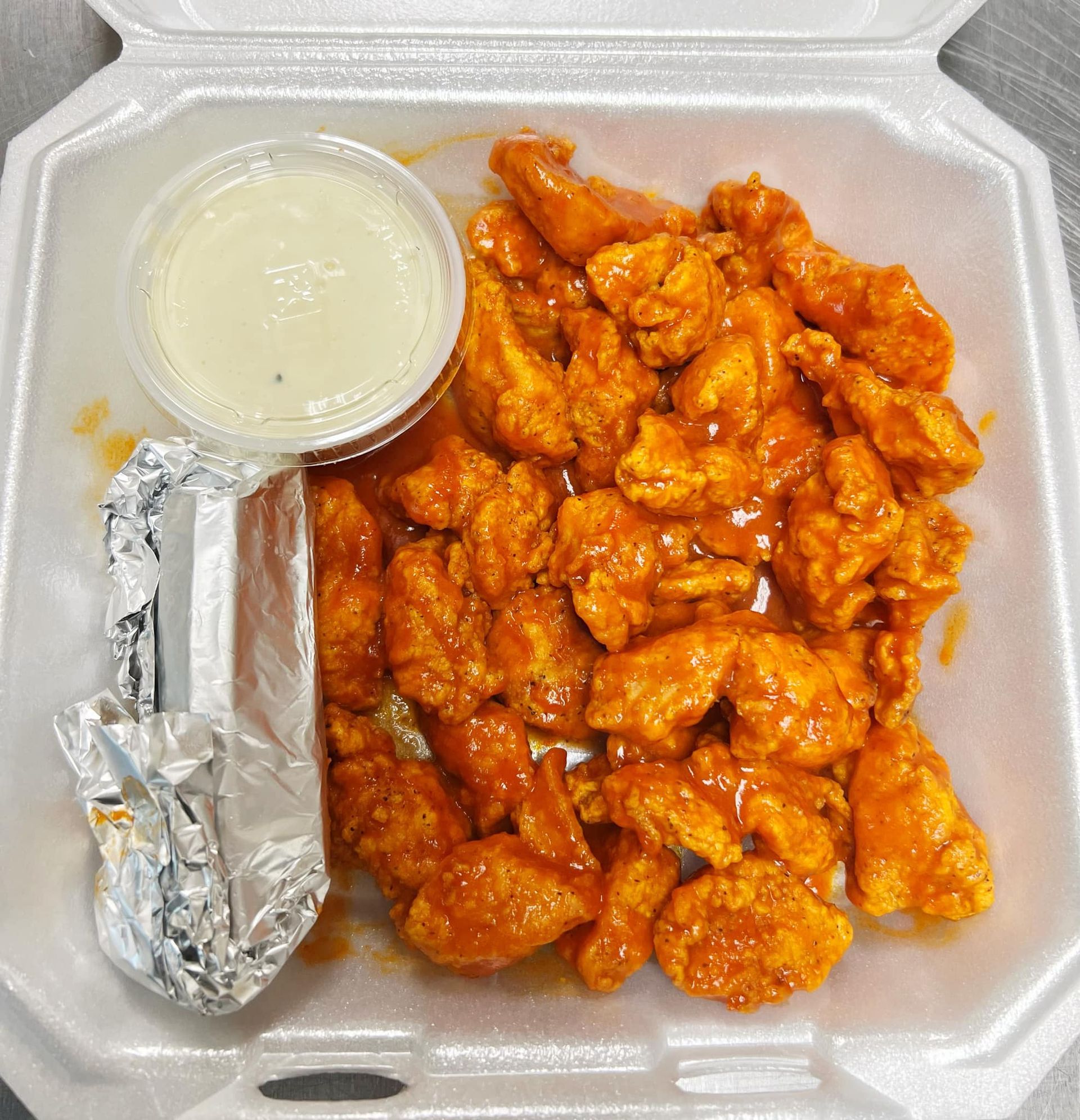 a styrofoam container filled with boneless wings and dipping sauce.