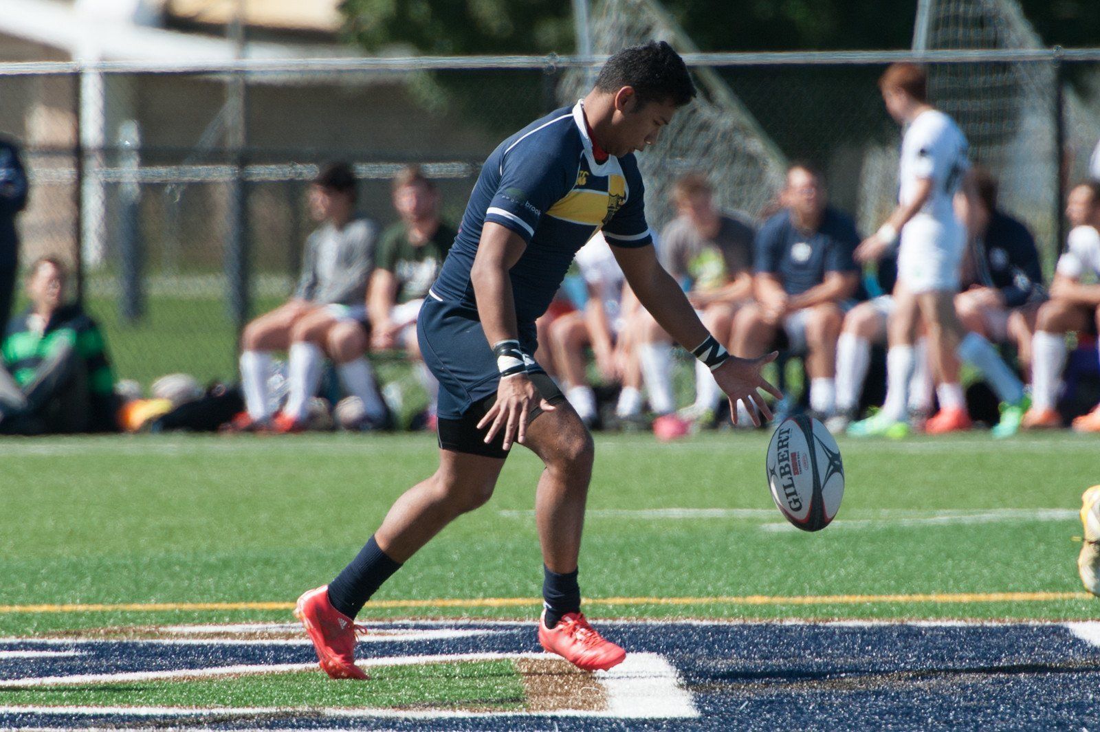 A man is kicking a rugby ball on a field.