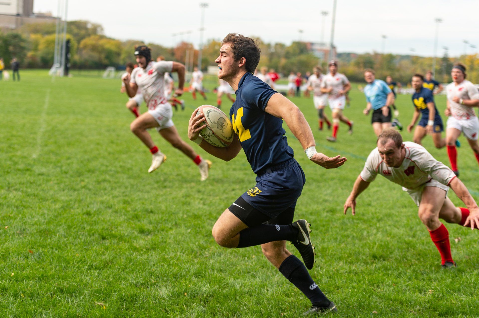 A man is running with a rugby ball on a field.