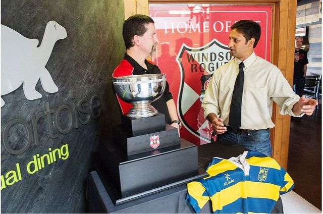 Two men are standing in front of a sign that says home of windsor rugby