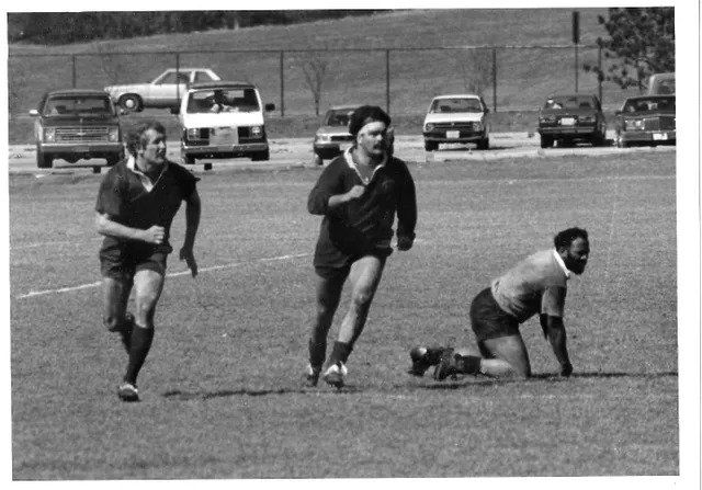 A black and white photo of three men running on a field