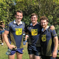 Three rugby players are posing for a picture on a field.