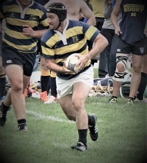 A man in a yellow and blue striped shirt is running with a rugby ball