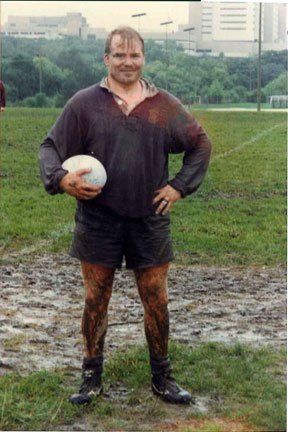 A man is standing on a muddy field holding a soccer ball.