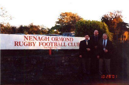 Men standing in front of a sign that says nenagh ormond rugby football club