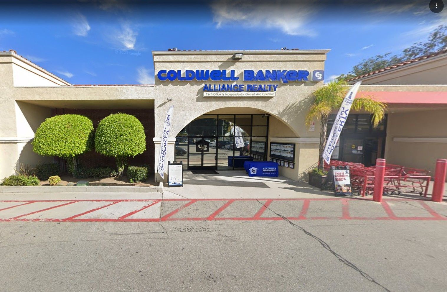 Coldwell Banker office entrance under a blue sky, with a sign and arched doorway.