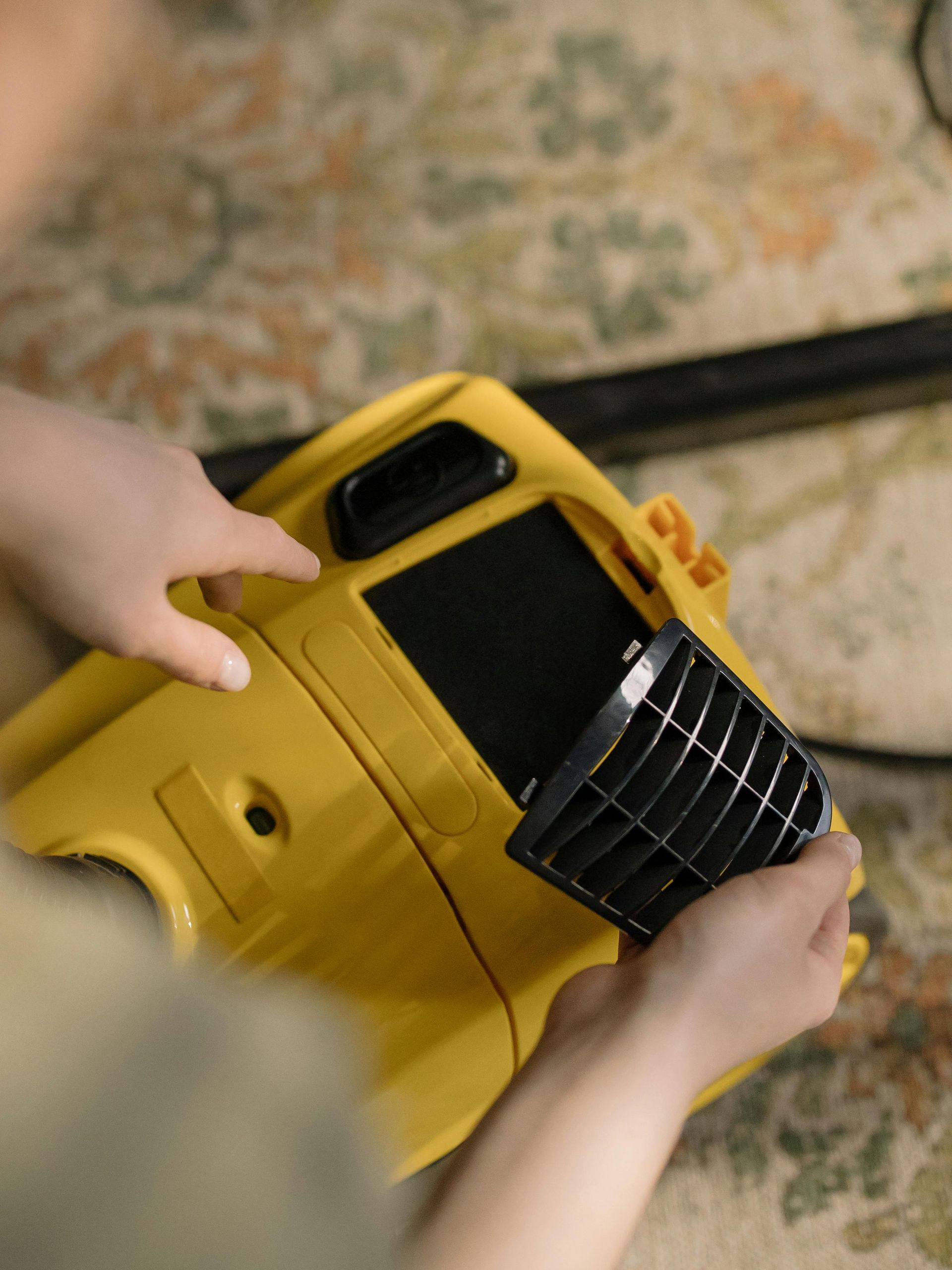 Person removes a black filter from a yellow vacuum cleaner.