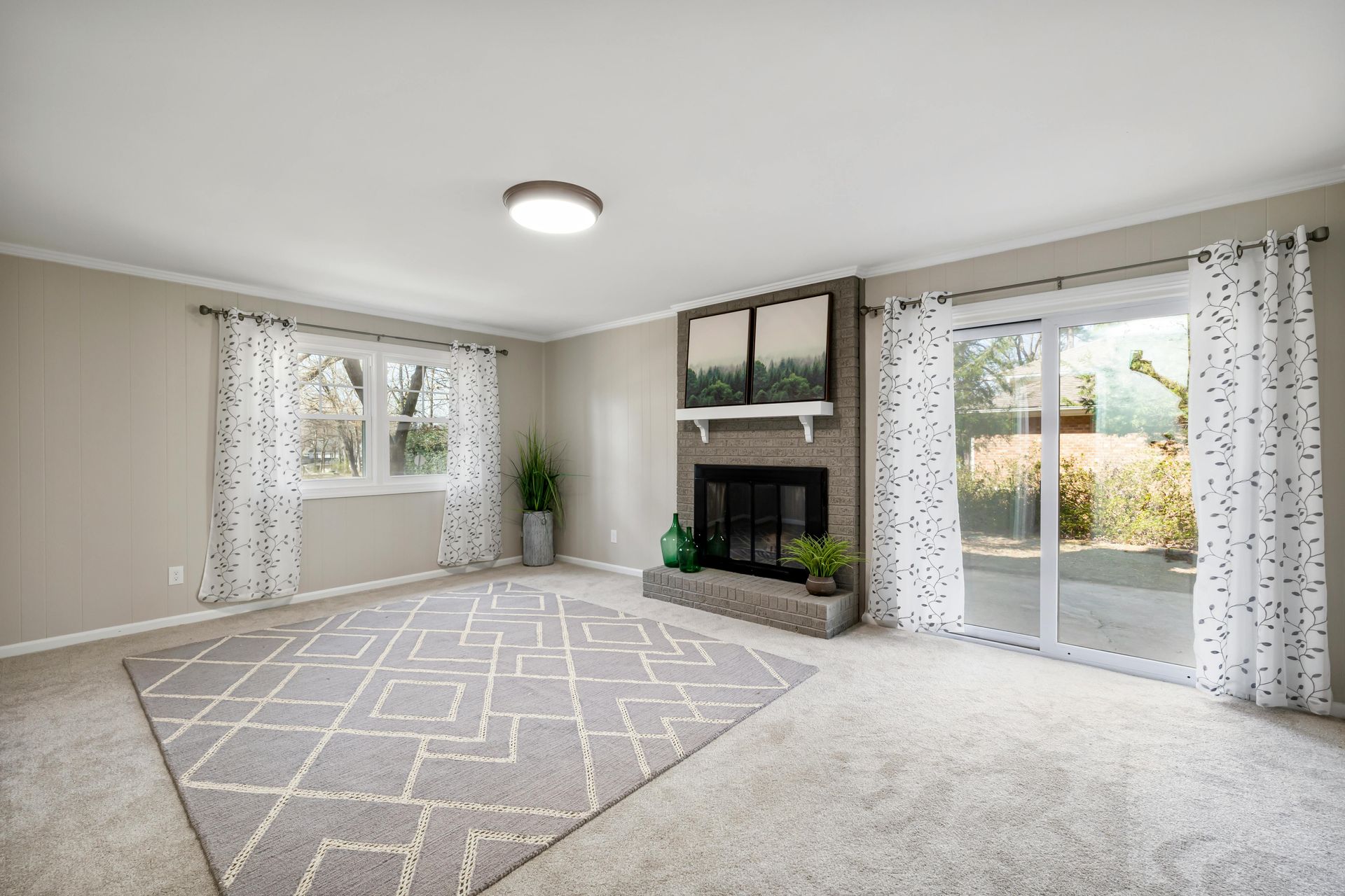 Empty living room with fireplace, sliding glass door, patterned rug, and curtains.