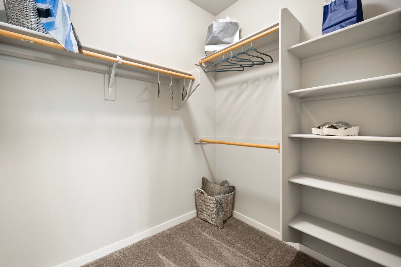 Walk-in closet with white shelves, wooden rods, and a woven basket on beige carpet.