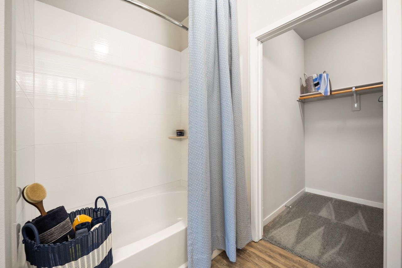Bathroom with white-tiled shower area and a nearby walk-in closet.