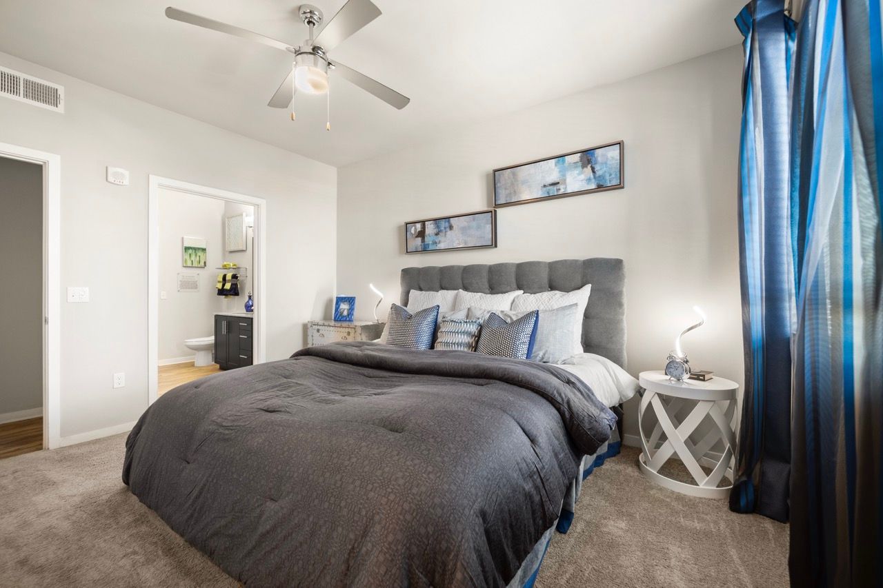 Cozy bedroom in a modern apartment with a gray upholstered bed, blue accents, and soft lighting.