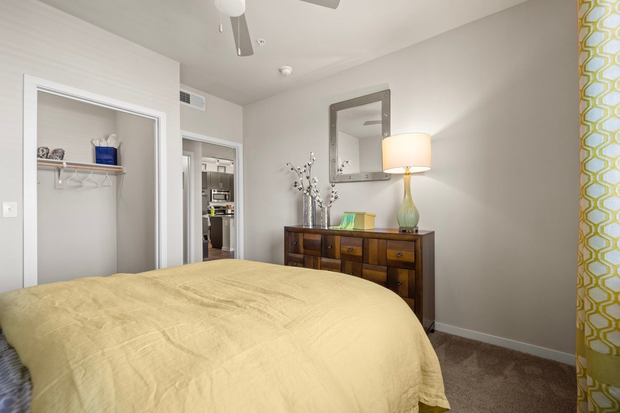 Bedroom with a bed covered by a yellow comforter, dresser, lamp, mirror, and open closet.