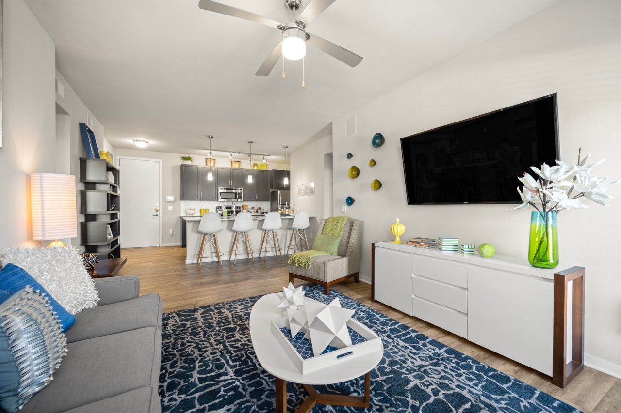 Open-concept living room with sofa, coffee table, wall-mounted TV, and kitchen bar.