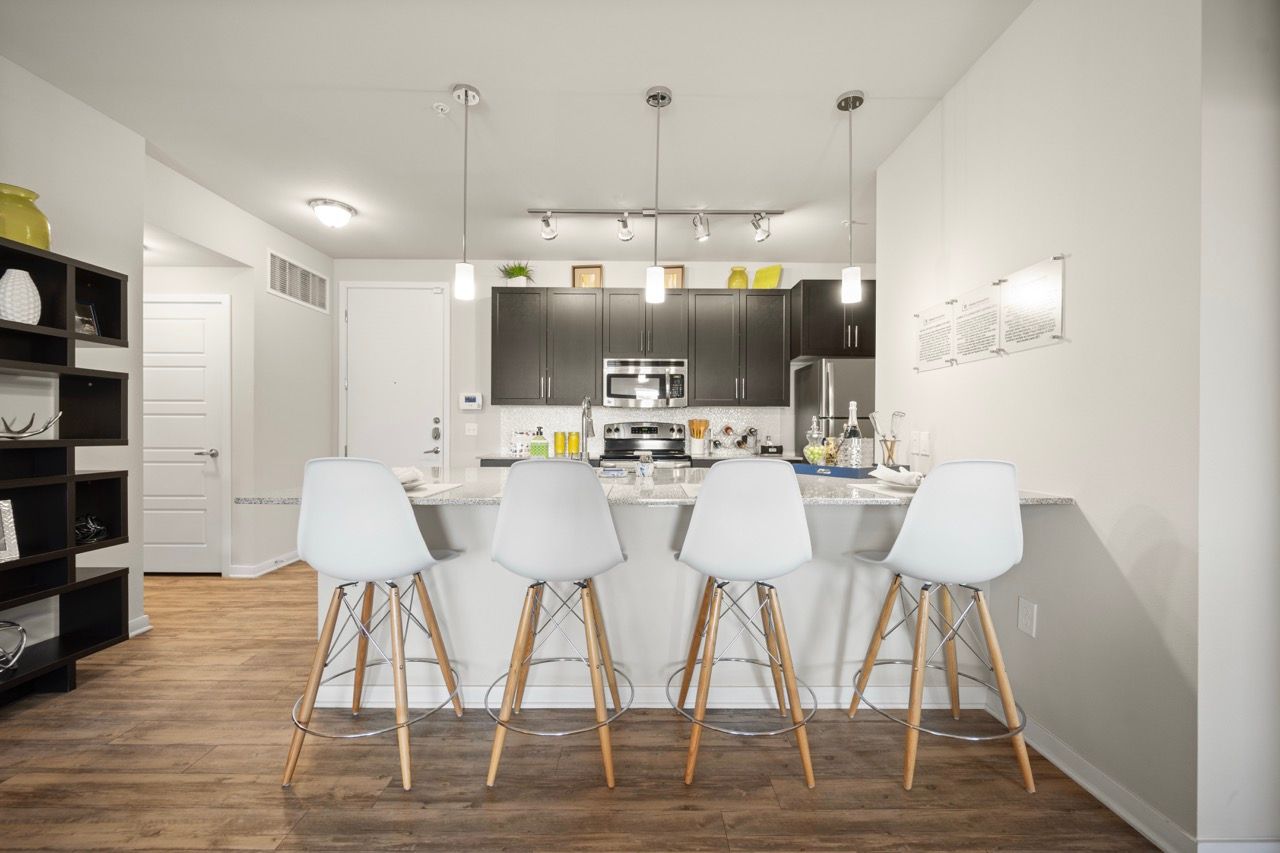Bright modern apartment kitchen with a granite island and five white bar stools.