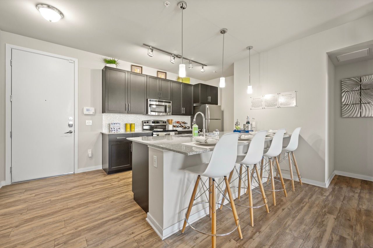 Open-concept kitchen with dark cabinets, stainless steel appliances, and a white island with bar stools.