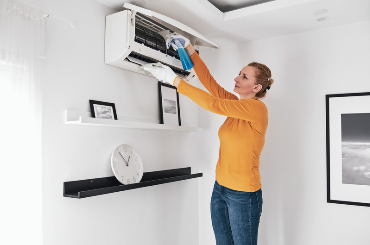 A woman cleaning her air conditioning unit for preventative maintanence.