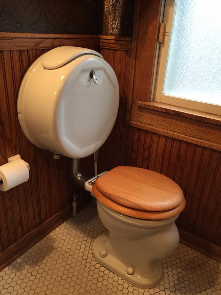 A toilet with a wooden seat sits in a bathroom next to a window