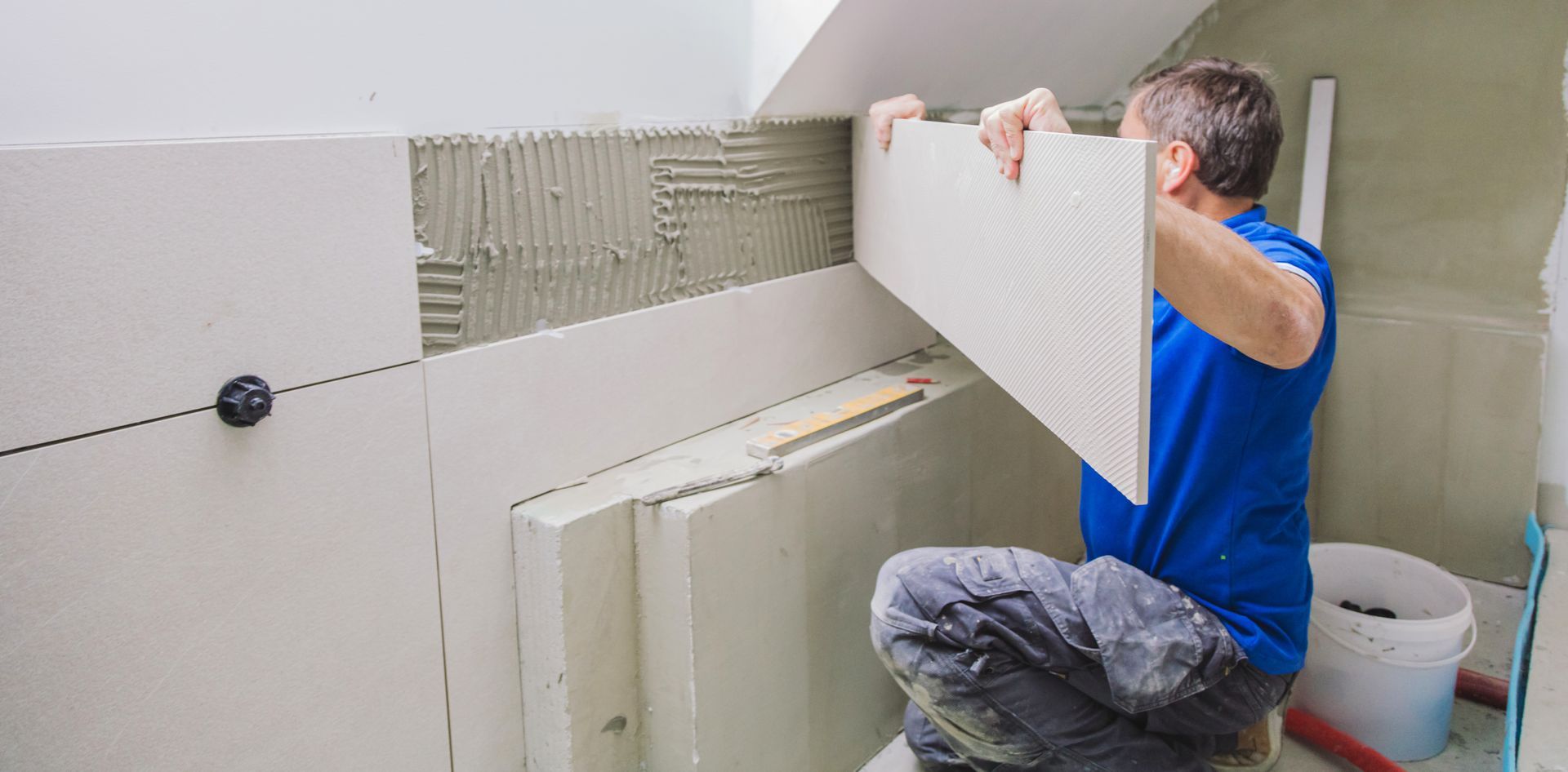 A man is kneeling down in a bathroom holding a tile.