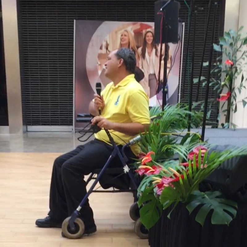 A man in a yellow shirt is sitting in a wheelchair holding a microphone