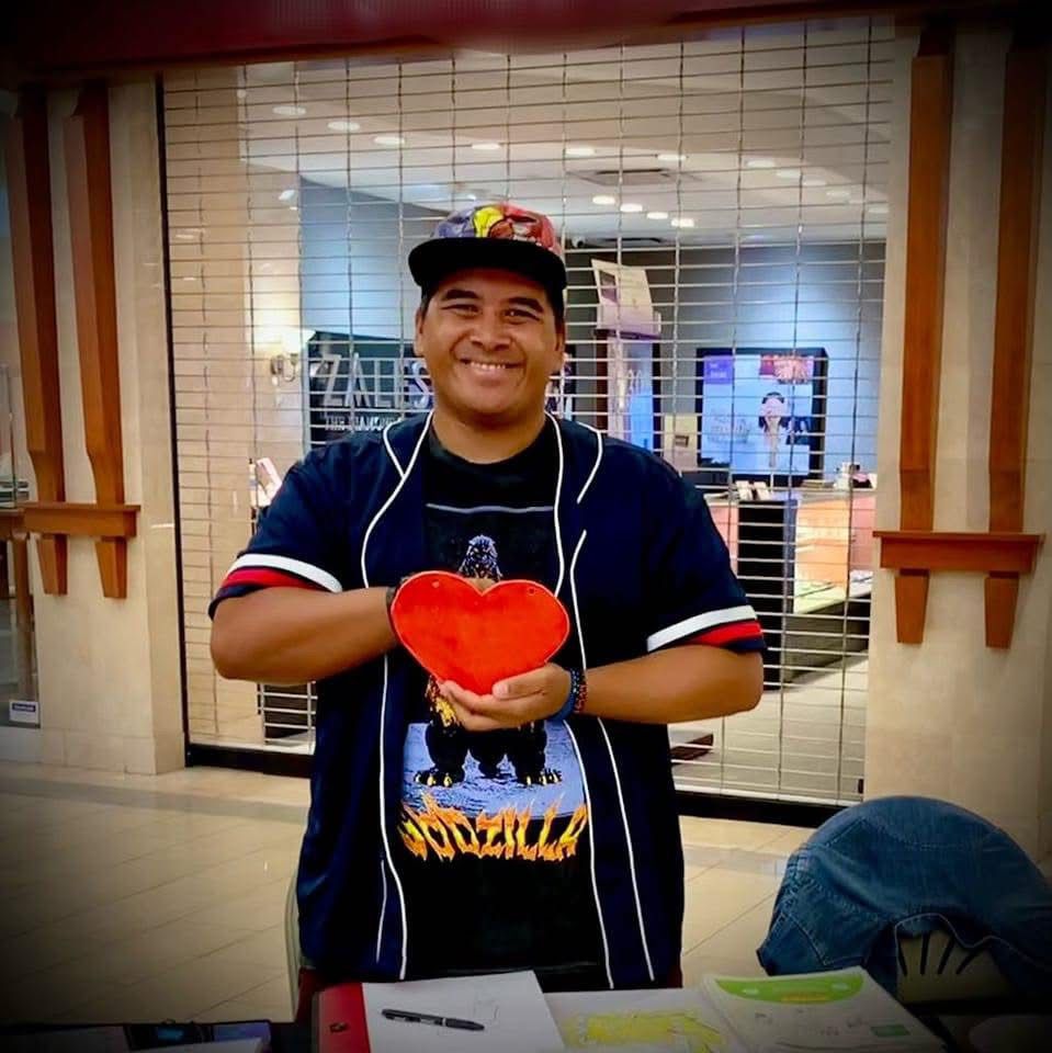 A man wearing a shirt that says godzilla is holding a red heart