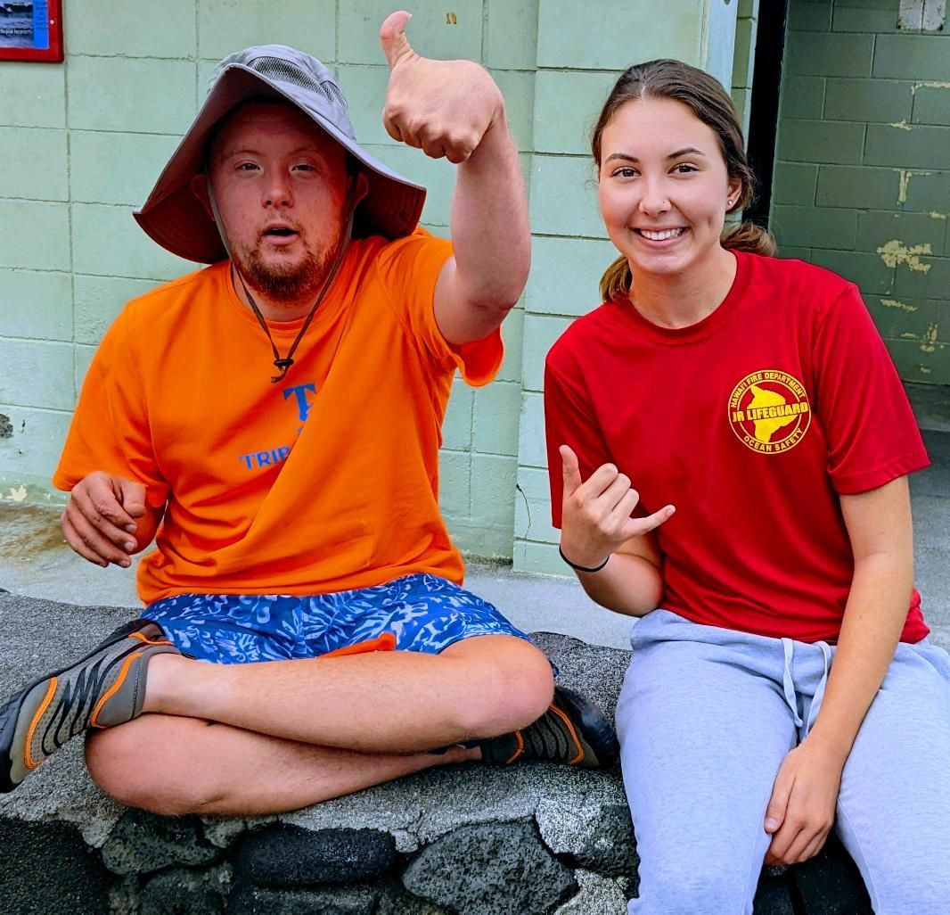A man and a woman are sitting next to each other and the man is wearing an orange shirt with the letter t on it