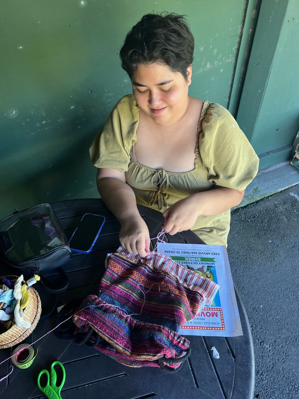 A woman is sitting at a table working on a backpack.